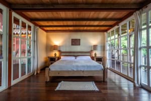Bedroom with large windows overlooking lush greenery and ocean in Dominical.