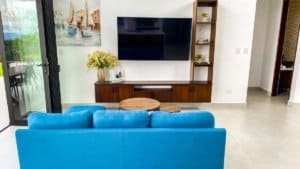 Bright living room with blue sofa, TV, and ocean view balcony.
