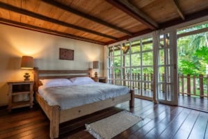 Bedroom with wooden ceiling and balcony overlooking lush greenery.
