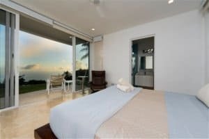 Bedroom with large glass doors overlooking the ocean and jungle canopy.