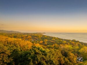 Scenic view of Dominical coastline with lush greenery and ocean at sunset.
