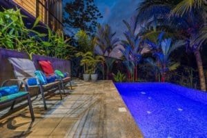 Poolside lounge chairs with colorful cushions and lush tropical plants at dusk.