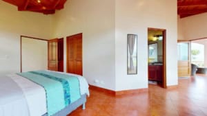 Bright bedroom with ocean view, wooden doors, and terracotta tiles.