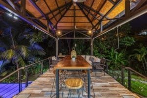 Outdoor dining space with wooden table and chairs in lush tropical setting.