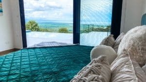 Interior of a bedroom with large glass doors showing ocean and mountain views.