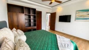 Spacious bedroom with green bedding, wooden furniture, and ocean view.