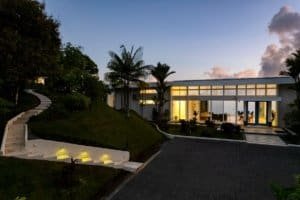 Modern estate with large glass windows, lush landscaping, and sunset sky in Dominical.