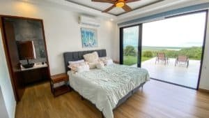 Modern bedroom with panoramic ocean and mountain views from large glass doors.