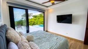 Modern bedroom with ocean view, sliding glass door, and flat-screen TV.