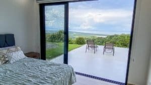 Bedroom with large glass doors opening to panoramic ocean and mountain scenery.