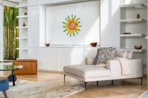 Bright living room with white walls, colorful sun wall art, and ocean view.