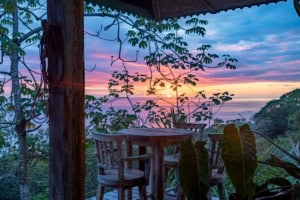 Scenic ocean view from a balcony with wooden furniture and lush greenery.