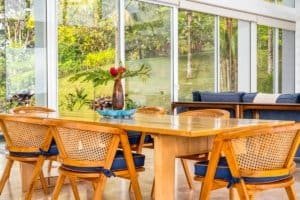 Bright dining space with wooden table and rattan chairs overlooking lush greenery.
