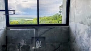 Modern bathroom with panoramic ocean and mountain view from window.