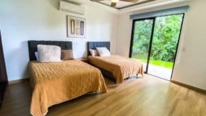 Spacious bedroom with two beds and large sliding glass door to nature.