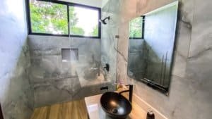 Contemporary bathroom with marble walls, wooden floor, and a black vessel sink.