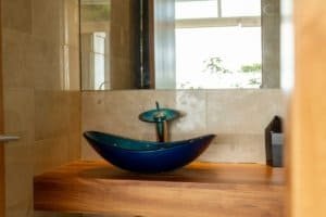 Elegant blue vessel sink with wooden countertop and mirror in bathroom.