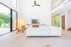 Bright living room with large windows, white furniture, and tropical scenery.