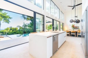 Bright kitchen with large windows overlooking lush greenery and pool area.