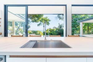 Contemporary kitchen with large windows overlooking lush tropical landscape and ocean.