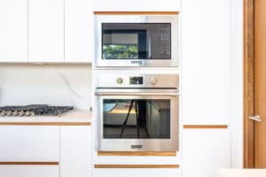 Contemporary kitchen with white cabinets, microwave, and oven setup.