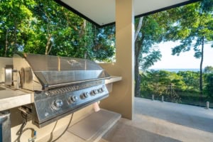 Balcony with stainless steel grill overlooking lush tropical forest and ocean.