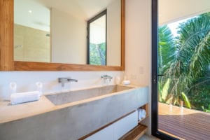 Modern bathroom with large mirror and sliding glass door to tropical balcony.