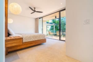 Modern bedroom with ocean view, balcony, and tropical surroundings.