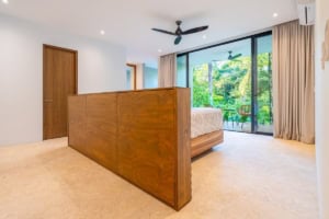 Spacious bedroom with large glass doors opening to tropical balcony and ocean view.