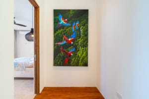 Vibrant parrot painting on white wall in tropical home interior.