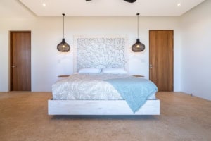 Modern bedroom with white bed, wooden doors, and hanging pendant lights.