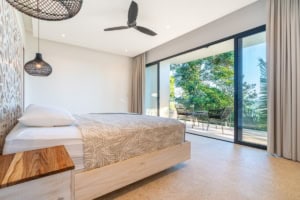 Modern bedroom with large glass doors overlooking tropical scenery and balcony.