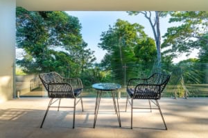 Outdoor balcony with two chairs and a small table overlooking lush greenery.