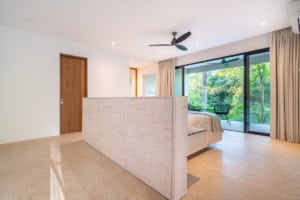 Spacious bedroom with large glass doors opening to lush greenery and ocean view.
