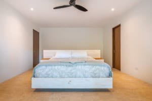 Spacious bedroom with white walls, wooden doors, and a large bed with blue bedding.