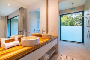 Modern bathroom with double sinks and ocean view through large window.