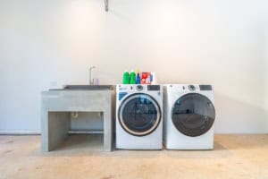 Laundry room with washing machine, dryer, and utility sink in tropical home.