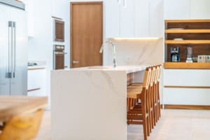 Contemporary kitchen with white cabinets, marble island, and wooden bar stools.