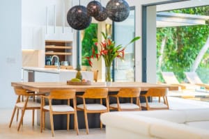 Bright tropical kitchen with wooden dining table and large glass doors.