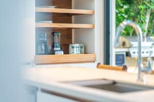 Contemporary kitchen with coffee maker, shelves, and view of greenery outside.