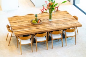 Elegant wooden dining table with eight chairs and tropical decor in bright room.