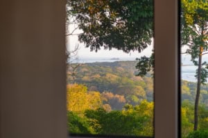 Scenic ocean view through window with lush green trees in Dominical, Costa Rica.