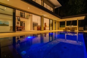Modern tropical home with infinity pool and outdoor lounge at night.