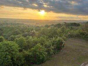 Beautiful sunset over lush green landscape with ocean and mountains in the distance.