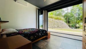 Interior of a bedroom with large glass doors overlooking lush greenery and a stone wall.