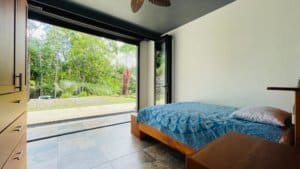 Bedroom with large glass door opening to lush green landscape.