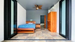Modern bedroom with wooden furniture, ceiling fan, and sliding glass doors to nature.