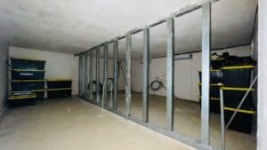 Interior of an unfinished underground room with metal framing and storage shelves.