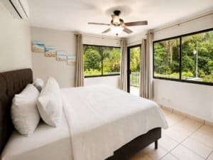 Bright bedroom with large windows overlooking lush garden in Dominical.