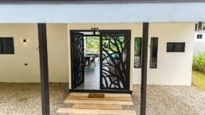 Modern home entrance with decorative black metal gate and tropical surroundings.